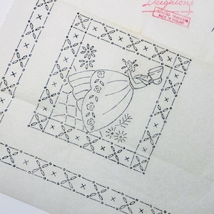 May include: A vintage embroidery transfer pattern on off-white paper featuring a black ink line drawing of a person in a dress holding flowers, surrounded by a geometric floral border. The text reads Deightons, Improved Transfer, Made in England, K373.