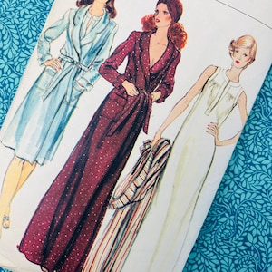 Può includere: Busta di modelli Vogue vintage con illustrazioni di tre donne in abiti lunghi e vestaglie. La copertina presenta la scritta "Vogue Patterns" in bianco. Gli abiti sono in azzurro, bordeaux a pois bianchi e bianco.