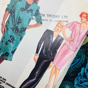 May include: A McCall's sewing pattern envelope featuring illustrations of three outfits: a teal dress with black abstract patterns, a black long-sleeved dress with a draped bodice, and a pink short-sleeved top paired with a matching pink skirt.