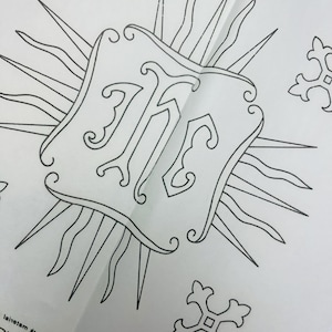 May include: Black and white heat transfer design featuring a stylized letter "M" within a decorative frame, surrounded by sunburst rays and cross-shaped embellishments. The design is printed on a translucent sheet.