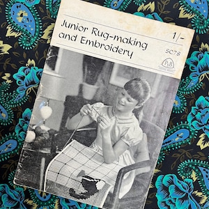 May include: Vintage book titled "Junior Rug-making and Embroidery" with a black and white image of a young person crafting. The book is set against a backdrop of a dark fabric with a teal and gold floral paisley pattern.