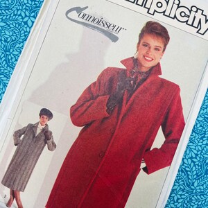 May include: A Simplicity Connoisseur Collection sewing pattern envelope featuring illustrations of a long, red, button-front coat with a high collar and a second version of the same coat in a grey herringbone pattern, both shown with dark gloves.