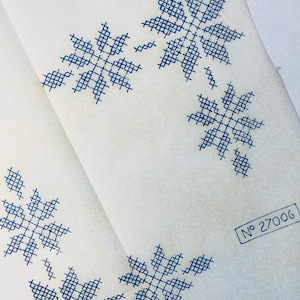 Könnte beinhalten: Nahaufnahme von weißem Stoff mit blauem Kreuzstich-Schneeflockenmuster. Das Design wiederholt sich über den Stoff. Die Nummer "27006" ist in einem kleinen Rechteck unten rechts aufgedruckt.