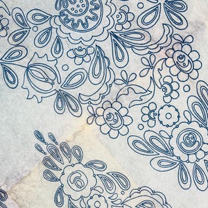 May include: A sheet of off-white transfer paper featuring a repeating dark blue ink outline of a floral pattern. The design consists of stylised flowers, teardrop shapes, and swirling lines arranged in a decorative, symmetrical composition.
