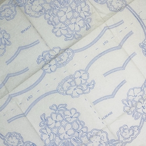 Op de afbeelding: Een beige naaipatroonvel met blauwe inktillustraties van bloemclusters en decoratieve randen. Het papier bevat gedrukte instructies met de woorden CUT en CREASE, samen met de tekst HOME WEEKLY W64C die aan de zijkant zichtbaar is.