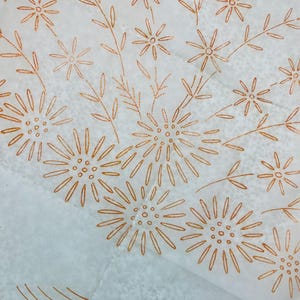 May include: A white fabric surface featuring a repeating pattern of embroidered copper-colored flowers and stems. The design consists of stylized daisy-like blossoms with thin petals and small circular centers, arranged in a delicate floral motif.