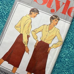 Op de afbeelding: Een Style naaipatroon-envelop met illustraties van een lichtgeel overhemd met lange mouwen en kraag en een donkerbruine midirok. De tekst op de envelop bevat het woord Style, de maten 10, 12, 14 en 16, en het label Pattern Patron.
