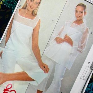 May include: A sewing pattern envelope featuring two white garment variations. One view shows a sleeveless white top with a sheer neckline and white cropped trousers. The other view displays a sheer white long-sleeved jacket over a white top and trousers.
