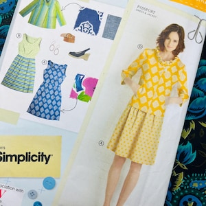 Può includere: Una busta per cartamodello Simplicity Lisette per un abito e una giacca Passport. La parte anteriore mostra illustrazioni di vari stili di abiti e giacche, tra cui un completo giacca e gonna giallo a motivi e disegni di abiti blu e verdi.