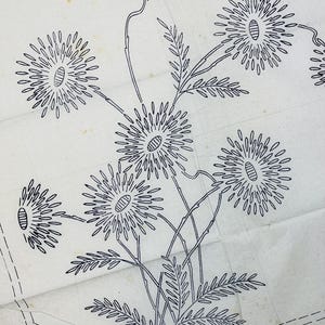 Op de afbeelding: Een vintage borduurtransferpatroon gedrukt op off-white papier met een zwarte lijnillustratie van een tros madeliefachtige bloemen met lange stelen en geveerde bladeren, omringd door een gestippelde rechthoekige rand.