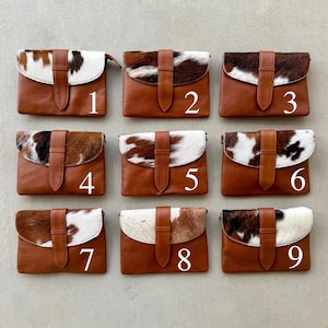 May include: Nine brown leather clutch bags with cowhide flap closures. Each bag has a different pattern of brown, black, and white cowhide. The bags are numbered 1 to 9.