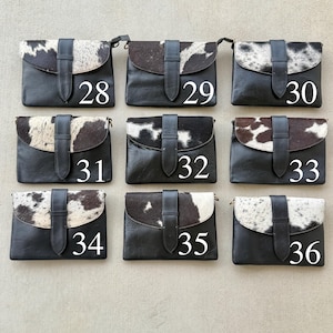 May include: Nine black leather crossbody bags with cowhide flap closures. Each bag has a black leather strap and a buckle closure. Numbers 28 to 36 are printed on the bags in white.
