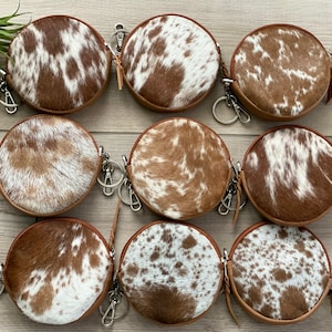 May include: Nine round brown and white cowhide leather coin purses with zipper closures and silver keychains.