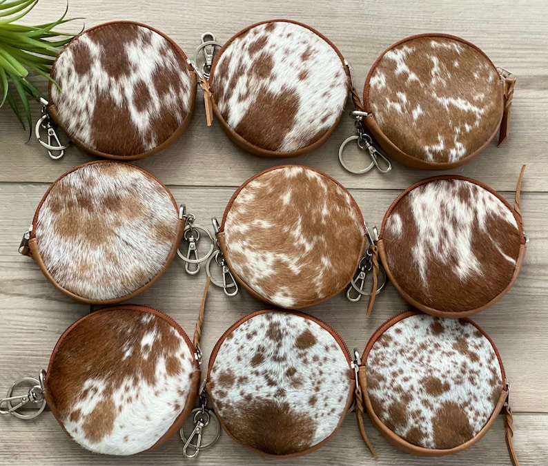 May include: Nine round brown and white cowhide leather coin purses with zipper closures and silver keychains.
