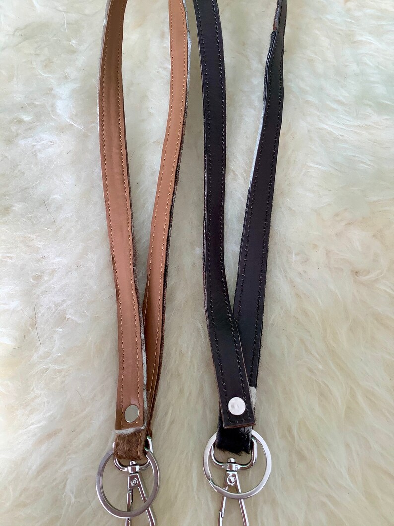 Op de afbeelding: Twee sleutelhangers met zilveren sleutelringen. De ene sleutelhanger is bruin met witte vlekken en de andere is van zwart leer.