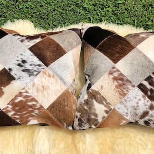 May include: Two square-shaped throw pillows with a diamond pattern made from patchwork cowhide. The pillows are brown, white, and black with a variety of patterns.