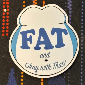 May include: White sticker with blue trim and the text "FAT and Okay with That!" in blue lettering.