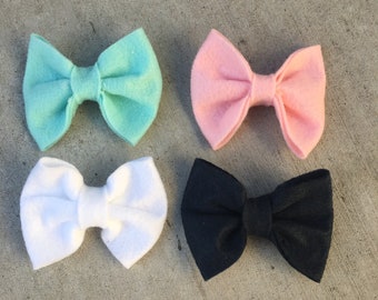 May include: Four felt bow hair clips in different colors: light blue, pink, white, and black.