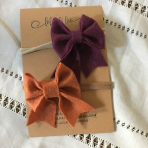 May include: Two felt hair bows on nude headbands. The bows are burgundy and burnt orange.