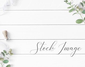 Feminine Flat Lay Styled with greenery, white ribbon, and stamp sealer on a white wood background.