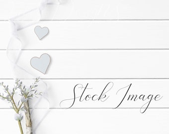 Feminine Flat Lay Styled with rustic white wood, blue hearts, flowers, and white ribbon on a white wood background.