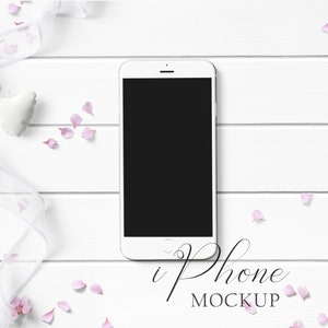 Puede incluir: Maqueta de iPhone blanco sobre un fondo de madera blanco con pétalos de flores rosas y una cinta blanca.
