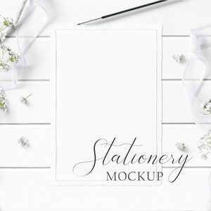 5x7 Stationery Mockup Styled with rustic wood, textured paper, flowers, white ribbon, and white wood pencil on a white wood background.