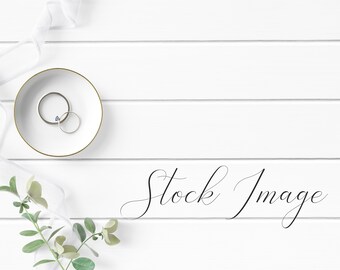 Feminine Flat Lay Styled with greenery, delicate cup, silver rings, and white ribbon on a white wood background.