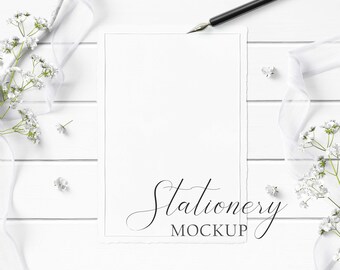 5x7 Stationery Mockup Styled with textured paper, flowers, white ribbon, and calligraphy pen and ink on a white wood background.