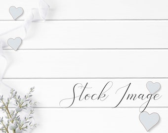 Feminine Flat Lay Styled with rustic white wood, rustic blue hearts, flowers, and white ribbon on a white wood background.