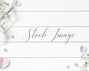 Feminine Flat Lay Styled with rustic white wood, white ribbon, pink paper hearts, and flowers on a white wood background.
