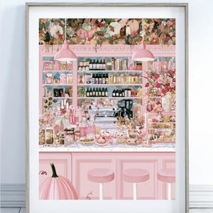 May include: A framed art print depicting a pink-themed cafe interior with a marble counter, stools, and shelves stocked with bottles and jars. The scene features a large pink pumpkin in the foreground, floral arrangements, and two hanging pendant lights.