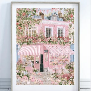 May include: A framed art print depicting a pink storefront with striped awnings, overflowing with floral arrangements and scattered pumpkins. The building features multiple windows, a central door, and black signage boards, all rendered in a soft, pastel colour palette with lush greenery and hanging bunting.
