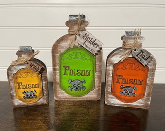 May include: Three wooden Halloween potion bottles with labels that read "Witch Potion", "Spider Venom", and "Toad Breath". Each bottle has a skull and crossbones graphic and the word "Poison" on the label.