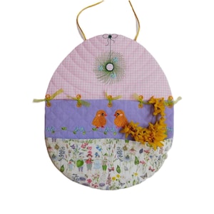 May include: A pink and purple quilted Easter egg-shaped wall hanging with embroidered birds and flowers. The egg is decorated with a gingham pattern and a floral design.