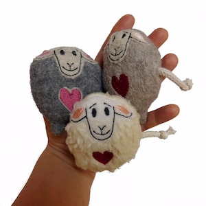 May include: Three plush sheep toys with embroidered faces and hearts. The sheep are grey, white, and brown.