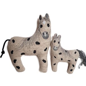 Könnte beinhalten: Zwei Plüschpferde, eines größer als das andere, sind aus hellbraunem Stoff mit schwarzen Flecken gefertigt. Beide Pferde haben gestickte Gesichter mit schwarzen Augen und einen weißen Stern auf der Stirn.