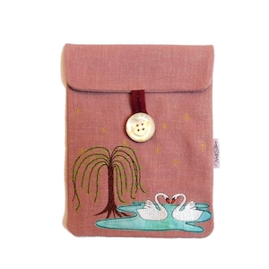 Könnte beinhalten: Eine rosa Leinen-Tasche mit einem weißen Knopfverschluss und gestickten Schwänen und einer Weide. Die Tasche hat ein kleines Etikett mit der Aufschrift "Nest Star".