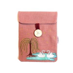 May include: A pink linen pouch with a white button closure and embroidered swans and a willow tree. The pouch has a small label that says "Nest Store".