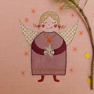 Könnte beinhalten: Gestickter Engel mit Flügeln, der einen Stern hält, auf einem rosa Hintergrund mit orangefarbenen Sternen.