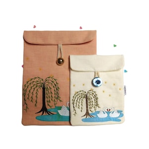 May include: Two fabric pouches with embroidered willow trees and swans. The larger pouch is peach colored and the smaller pouch is cream colored.