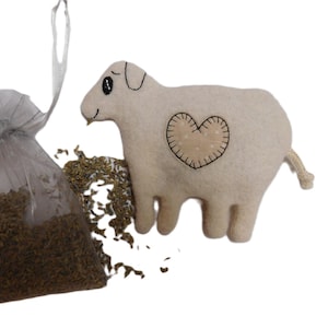 May include: A white felt sheep with a stitched heart on its side. The sheep is next to a small white bag filled with dried herbs.