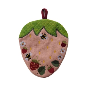 May include: A strawberry-shaped pot holder with a quilted green top and a pink body. The pink body features embroidered strawberries, bees, and white flowers. A burgundy loop is attached for hanging.