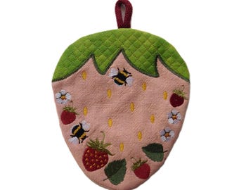 May include: A strawberry-shaped pot holder with a quilted green top and a pink body. The pink body features embroidered strawberries, bees, and white flowers. A burgundy loop is attached for hanging.
