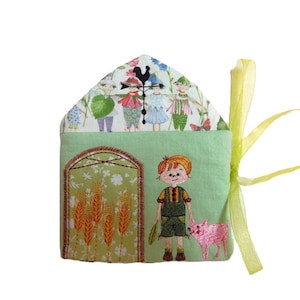 May include: A green fabric house-shaped pouch with a yellow ribbon. The front of the pouch features embroidered images of a boy holding a bunch of wheat, a pig, and a farmhouse with a window and wheat stalks. The top of the pouch features a white fabric with embroidered images of children and a weather vane.