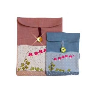 May include: Two fabric pouches with embroidered bleeding heart flowers. The larger pouch is pink and the smaller pouch is blue. Both pouches have a button closure.