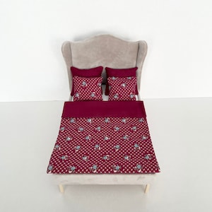 Könnte beinhalten: Ein Bettwäsche-Set mit burgunderfarbenem und weißem Blumenmuster mit zwei burgunderfarbenen Kissen auf einem weißen, gepolsterten Kopfteil.