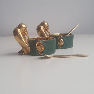 May include: Two small green ceramic salt and pepper shakers with gold bird-shaped handles and gold spoons.