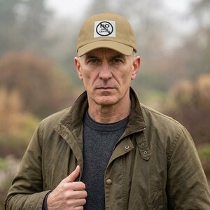 May include: A tan baseball cap featuring a white square patch on the front with the black text NO DARA CENTER and a circular graphic design. The cap has a curved brim and a structured crown, providing a classic look for casual outdoor wear.
