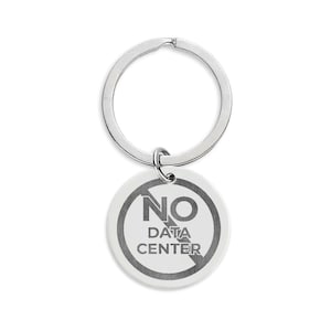 May include: A silver-toned metal keychain featuring a circular pendant. The pendant displays a circular prohibition symbol with a diagonal line through it, surrounding the text NO DATA CENTER in a bold, dark, sans-serif font on a light background.